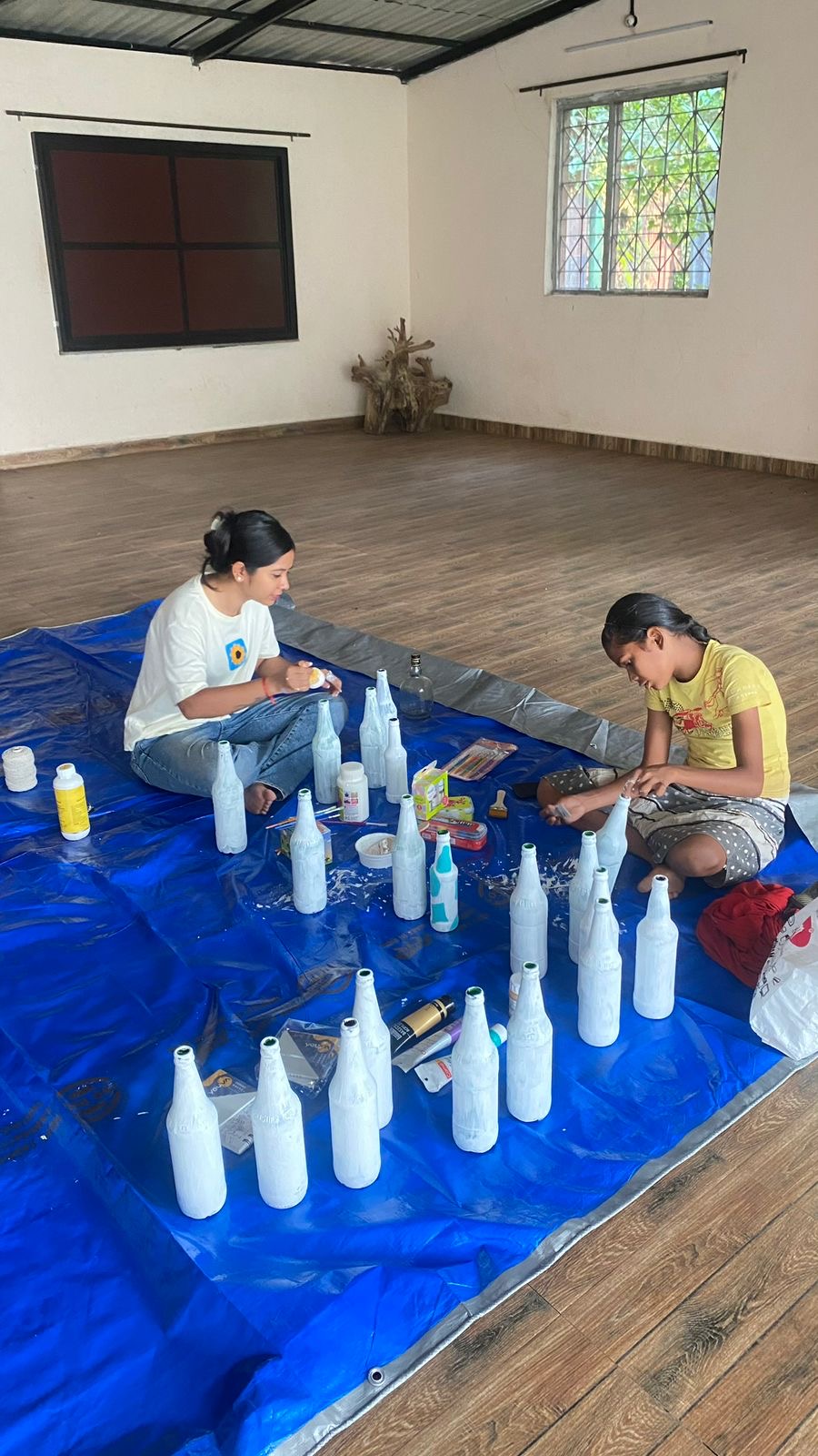 Two people painting white bottles
